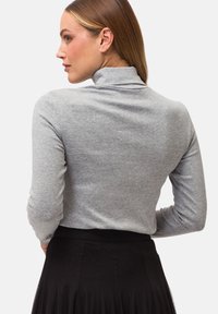 Grauer langärmeliger Rollkragenpullover, aus einem Baumwollmix, eng anliegendes Design, glatte Textur, kombiniert mit einem schwarzen Faltrock. Rückansicht gezeigt.