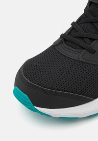 Chaussure de sport noire avec une tige en mesh texturé, présentant des accents turquoise sur la semelle et une semelle intermédiaire blanche. Lacets passés à travers des œillets.