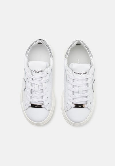 Baskets blanches en cuir avec des accents argentés, lacets plats, un panneau latéral texturé et un logo sur la languette avec un design à bout rond.