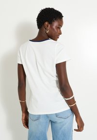 Camiseta blanca de algodón con cuello azul marino, mangas cortas y corte relajado, combinada con unos vaqueros de mezclilla azul claro.