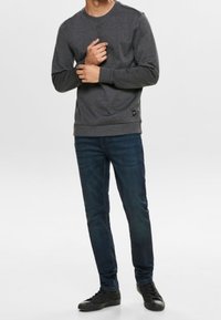 Grijze sweatshirt met een ronde hals en ribgebreide boorden, gecombineerd met donkerblauwe jeans en zwarte sneakers. Eenvoudig ontwerp, geen zichtbare patronen.