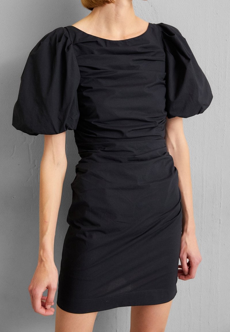 Svart fitted klänning med korta puffärmar, rynkad textur och fyrkantig halsringning. Tillverkad av ett mjukt, stretchigt tyg.