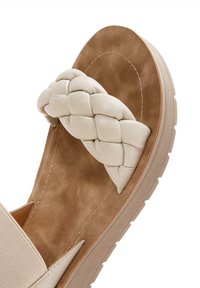 Sandal beige chiaro con una cintura in pelle intrecciata e una soletta in camoscio. Presenta una suola in gomma robusta con una leggera sagomatura.