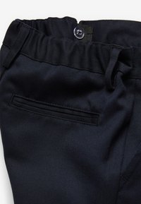 Pantalons bleu marine foncé avec une texture tissée, ceinture élastique et une poche arrière unique. Présente une fermeture à bouton et un design à plat sur le devant.