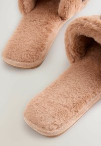 Mysiga beige tofflor i mjuk, plyschig textur och med öppen baktill. Sålen verkar vara tjock och något dämpad för komfort.