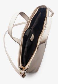 Beige leather handbag with a zip closure, smooth texture, and gold hardware accents. Interior features a black lining and dual compartments.