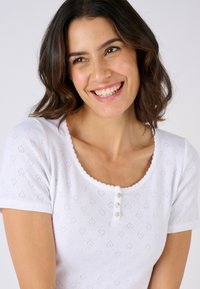 Top blanco de manga corta con escote festoneado, cierre de botones y sutiles patrones de corazones en toda la tela de punto.