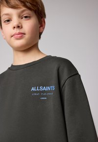 Mörkgrön sweatshirt med ribbad halsringning, med blå texten "ALLSAINTS" och extra text på japanska. Mjuk textur.