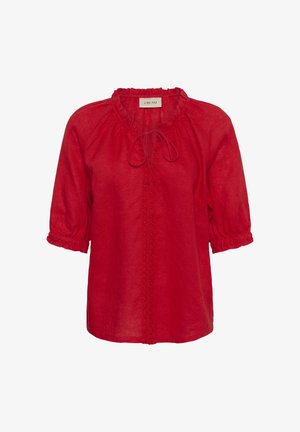 Blouse en lin rouge avec manches trois-quarts, col à volants, nouée à l'avant, et coutures décoratives verticales au centre.