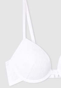 Reggiseno bianco in pizzo con coppe imbottite, spalline regolabili e dettaglio a fiocco al centro. Texture liscia e motivo floreale su tutta la superficie.