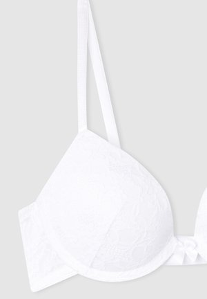 Reggiseno bianco in pizzo con coppe imbottite, spalline regolabili e dettaglio a fiocco al centro. Texture liscia e motivo floreale su tutta la superficie.