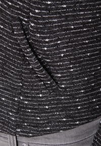 Dzianina w czarno-białe paski, z teksturowaną powierzchnią o nieco puszystym wyglądzie. Zawiera detal w postaci bocznego szwu.