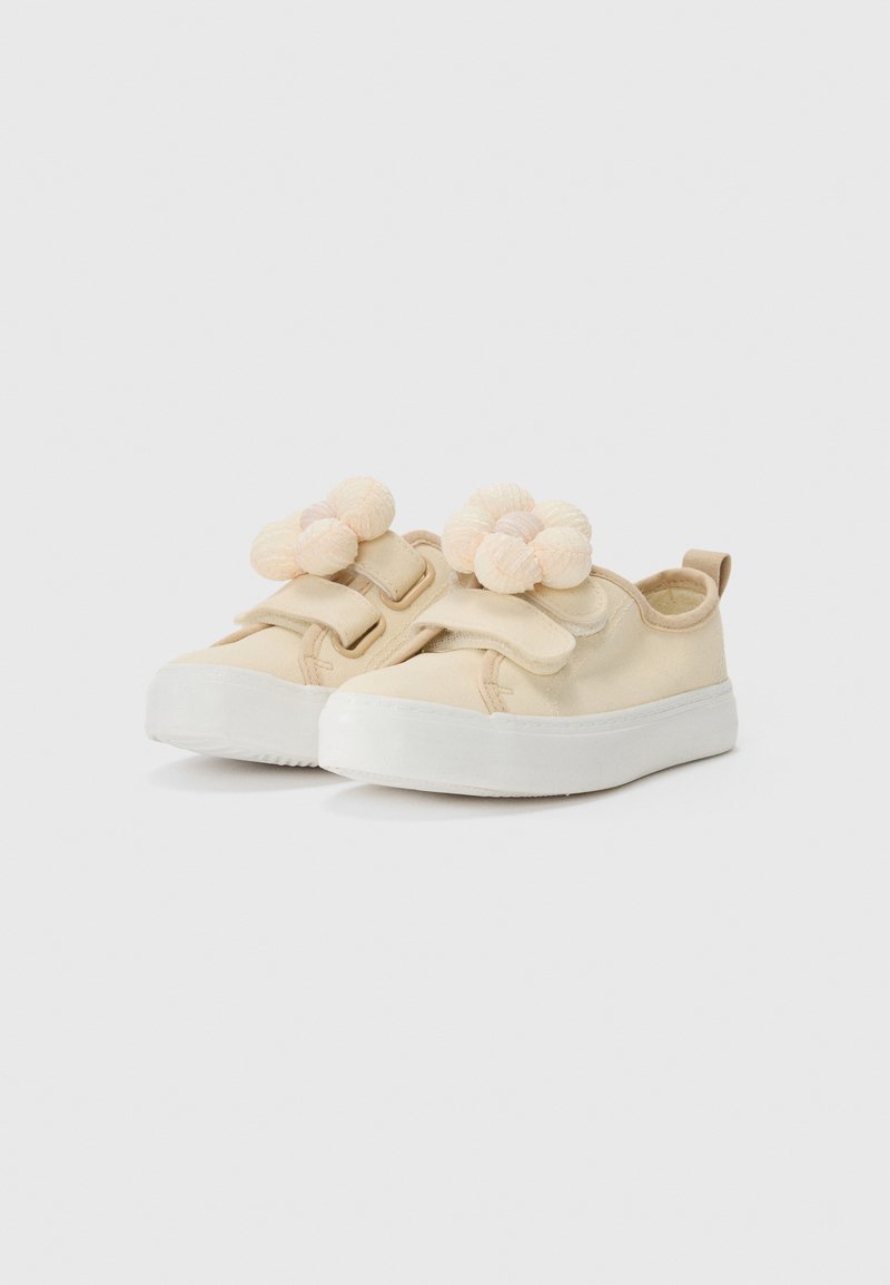 Beige Leinenschuhe mit einer strukturierten weißen Gummisohle, ausgestattet mit Klettverschlüssen und zwei dekorativen beigen und rosa flauschigen Akzenten auf der Vorderseite.