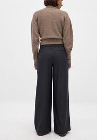 Beige gebreide trui met een hoge kraag, gecombineerd met donkergrijze wijde broek met een elastische tailleband en een gladde stoftextuur.