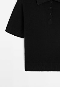 Mustassa neulotussa lyhythihaisessa polo-paidassa on kaulus, viiden napin suljenta ja ribbaus helmassa sekä hihojen reunoissa. Pehmeä rakenne.