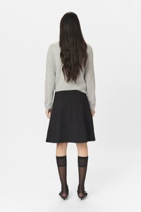 Pull long gris à manches longues associé à une jupe flare noire. Le mannequin porte des chaussettes noires à motifs montantes et des chaussures noires à petits talons.