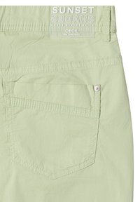 Light green pants back pocket with visible stitching and a label above reading "SUNSET SHADES UNDER DESERT SKIES CECIL We love pants."