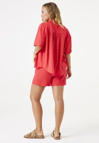 Rood T-shirt met korte mouwen, een losse pasvorm en een rugplooi, gecombineerd met bijpassende rode shorts. Het model draagt beige slidesandalen.