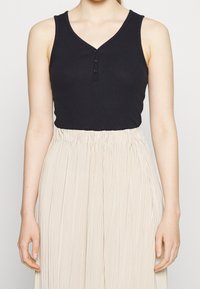 Black sleeveless top with a V-neck and three-button front detail, paired with a light beige pleated skirt, showcasing a soft texture.