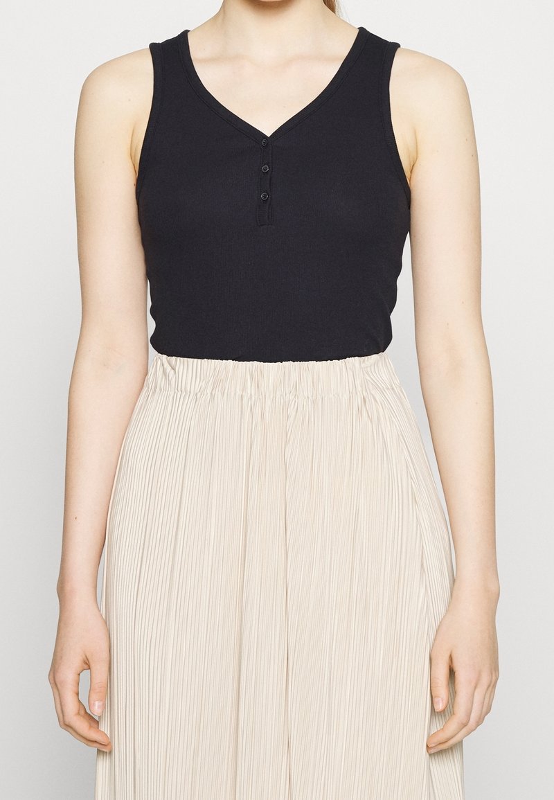 Black sleeveless top with a V-neck and three-button front detail, paired with a light beige pleated skirt, showcasing a soft texture.