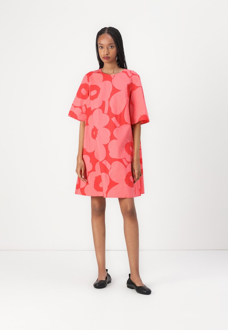 Red floral dress with short sleeves and a relaxed fit, featuring large pink flower patterns. Paired with black flats.