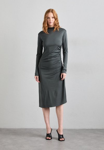 Dark gray, long-sleeve dress with textured ruching on the side, knee-length, made from a smooth material. Black open-toe heels.