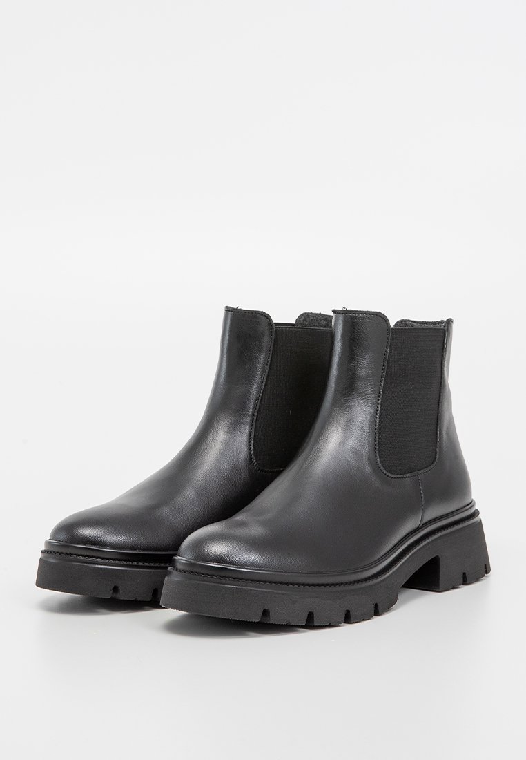 Botas de cuero negro hasta el tobillo con paneles laterales elásticos, suela de goma plana, punta redonda y un acabado suave. El diseño presenta acentos minimalistas.