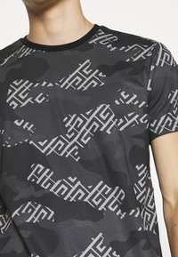 Grafické tričko s černým a šedým maskáčovým vzorem, geometrickými bílými akcenty a černým ribbovým kulatým výstřihem. Krátké rukávy.