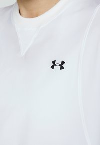 Gros plan d'un sweat-shirt blanc à col rond avec le logo noir Under Armour sur la poitrine et des coutures visibles.