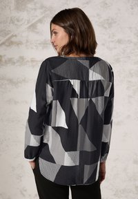 Blouse à manches longues en noir et gris avec un motif géométrique, à coupe décontractée, présentant des textures variées et un détail de pli au dos.