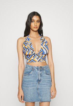 Top cropped halter com estampa geométrica colorida em azul, laranja e cinza; combinado com uma saia de denim azul claro, com bainha desfiada e bolsos frontais.