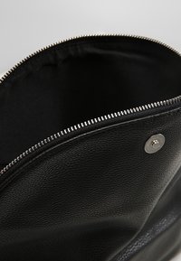 Borsa in pelle nera con chiusura a zip. Interno foderato in tessuto nero. Presenta un bottone a pressione argentato e una superficie esterna testurizzata per una migliore presa.