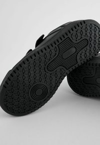 Semelles en caoutchouc noir de chaussures avec des motifs de semelle hexagonaux et circulaires sur un fond gris clair.