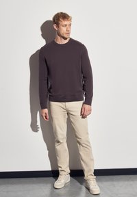 Dunkelpurpurnes Crewneck-Sweatshirt, beige Hose und hellfarbige Sneakers. Glatte Stoffoberfläche, gerippte Bündchen und ein dezentes Logo auf der Brust.
