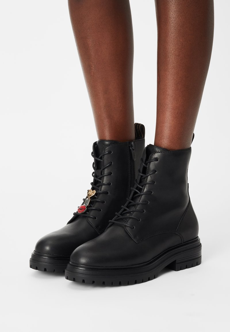 Bottines en cuir noir avec un design à lacets, dotées d'accents décoratifs de charms, d'une semelle robuste et d'une fermeture éclair pour un enfilage facile.