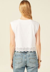 Witte cropped top met korte mouwen, voorzien van een kanten rand aan de onderkant. Gecombineerd met lichtblauwe high-waisted jeans.