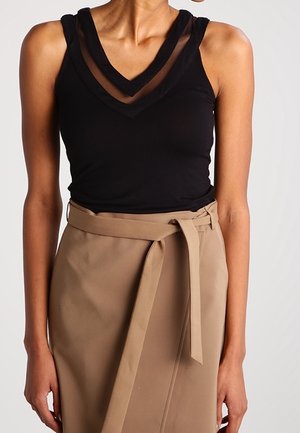 Zwarte mouwloze top met gelaagde transparante V-hals, gecombineerd met een beige rok met hoge taille en een geknoopt riemaccent.