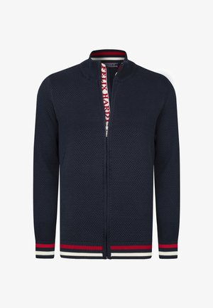 Cardigan zippé texturé bleu marine avec col montant, poignets et ourlet rayés rouge et blanc, et texte « Felix Hardy » sur la doublure intérieure du zip.