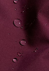 Bourgogne tyg med en slät yta, som har flera vattendroppar som vilar på ytan och reflekterar ljus.