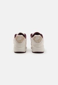 Baltas un bordo Nike Air sporta apavi ar teksturētu zamša papēdi, mīkstu apkakli un redzamu gaisa amortizāciju zole.