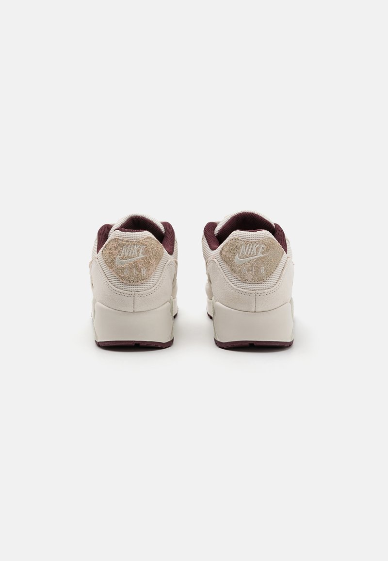 Witte en bordeaux Nike Air sneakers met een gestructureerde suede hak, een gewatteerde kraag en zichtbare Air demping in de zool.