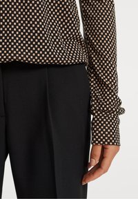 Långärmad topp med svart och beige rutig mönster, med mjuk textur, kombinerad med svarta högmidjade byxor.