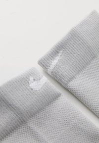 Grau sportliche Socken mit gerippter Textur, die weiße Logo-Details an den Bündchen aufweisen. Das Material scheint atmungsaktiv und dehnbar für Komfort zu sein.