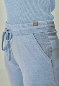 Hellblaue Jogginghosen mit einem gerippten Taillengummi, Zugband und gestrickter Textur sowie seitlichen Taschen. Dezenter Logopatch angebracht.