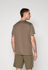 T-shirt à manches courtes, col rond, en tissu marron foncé, associé à un short vert olive. Texture lisse, design minimaliste, sans logos visibles.