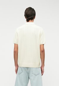 Πόλο μπλούζα κοντομάνικη, πλεχτή με ρίγες σε εκρού απόχρωση, διαθέτει κλασικό γιακά και ευθύ στρίφωμα, συνδυασμένο με ανοιχτό μπλε τζιν παντελόνι.