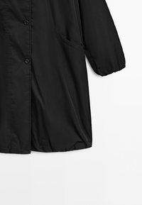 Black long-sleeve coat with button closure, elastic cuff, and side pocket, shown from midsection to hem on white background.