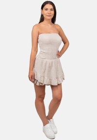 Strapless, lichtbeige mini-jurk met een gesmokt bovenstuk, een gerimpelde zoom en een textielstof. Gepaard met witte sportschoenen.