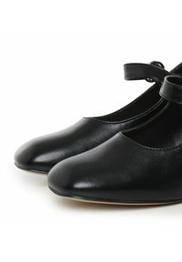 Zapatos de ballet de cuero negro con punta redonda y correa en el tobillo. Textura suave y diseño minimalista, sin hardware o adornos visibles.