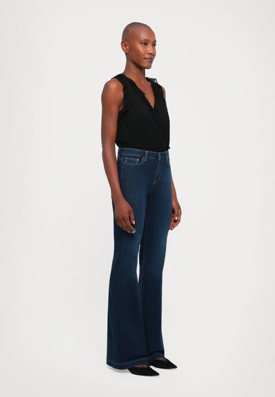 Svart ärmlös topp med volangdetaljer, ihop med mörkblå utsvängda jeans. Jeansena har en rak midja och subtil sömnad.